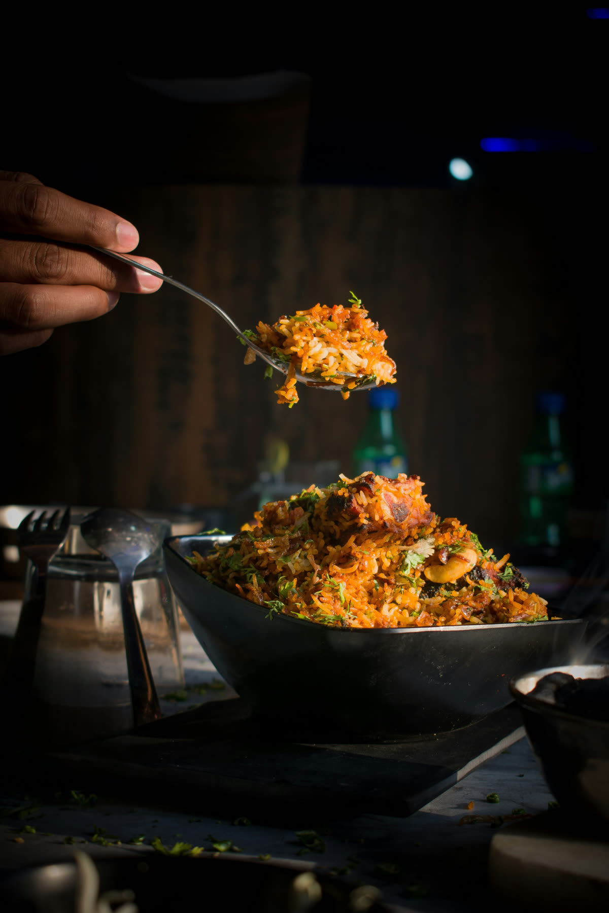 A spoonful of biryani lifted from a heaping bowl garnished with cilantro
