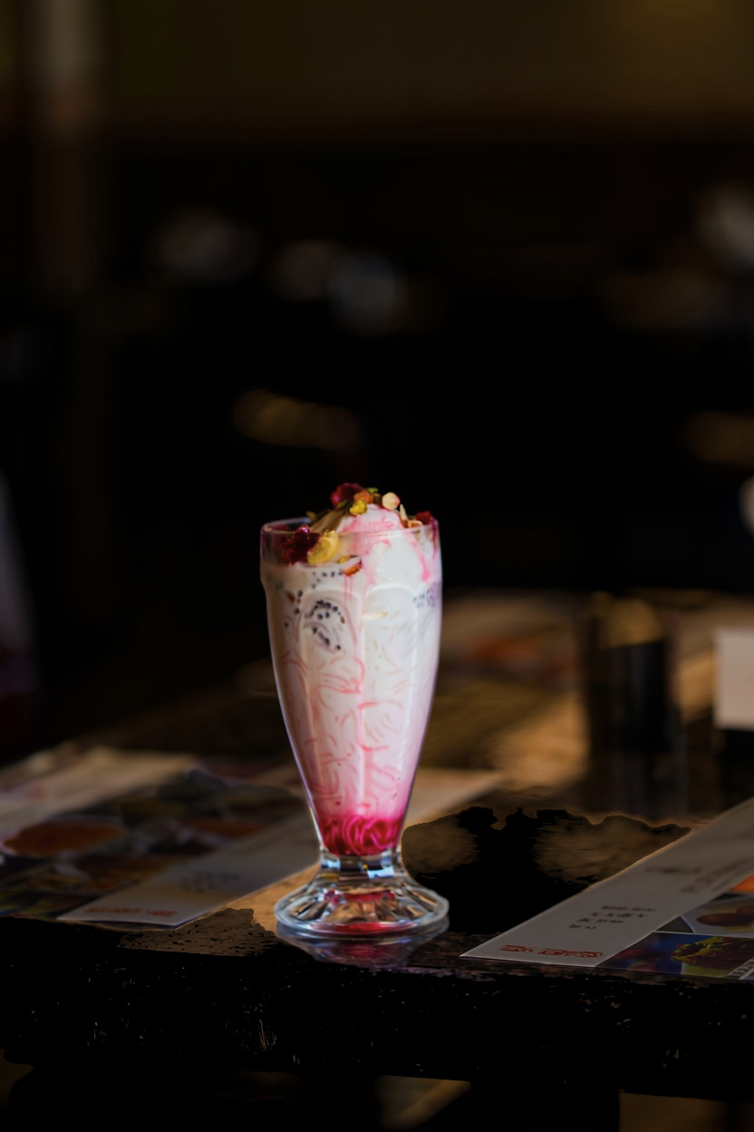 A tall glass of falooda topped with ice cream, rose petals and pistachios
