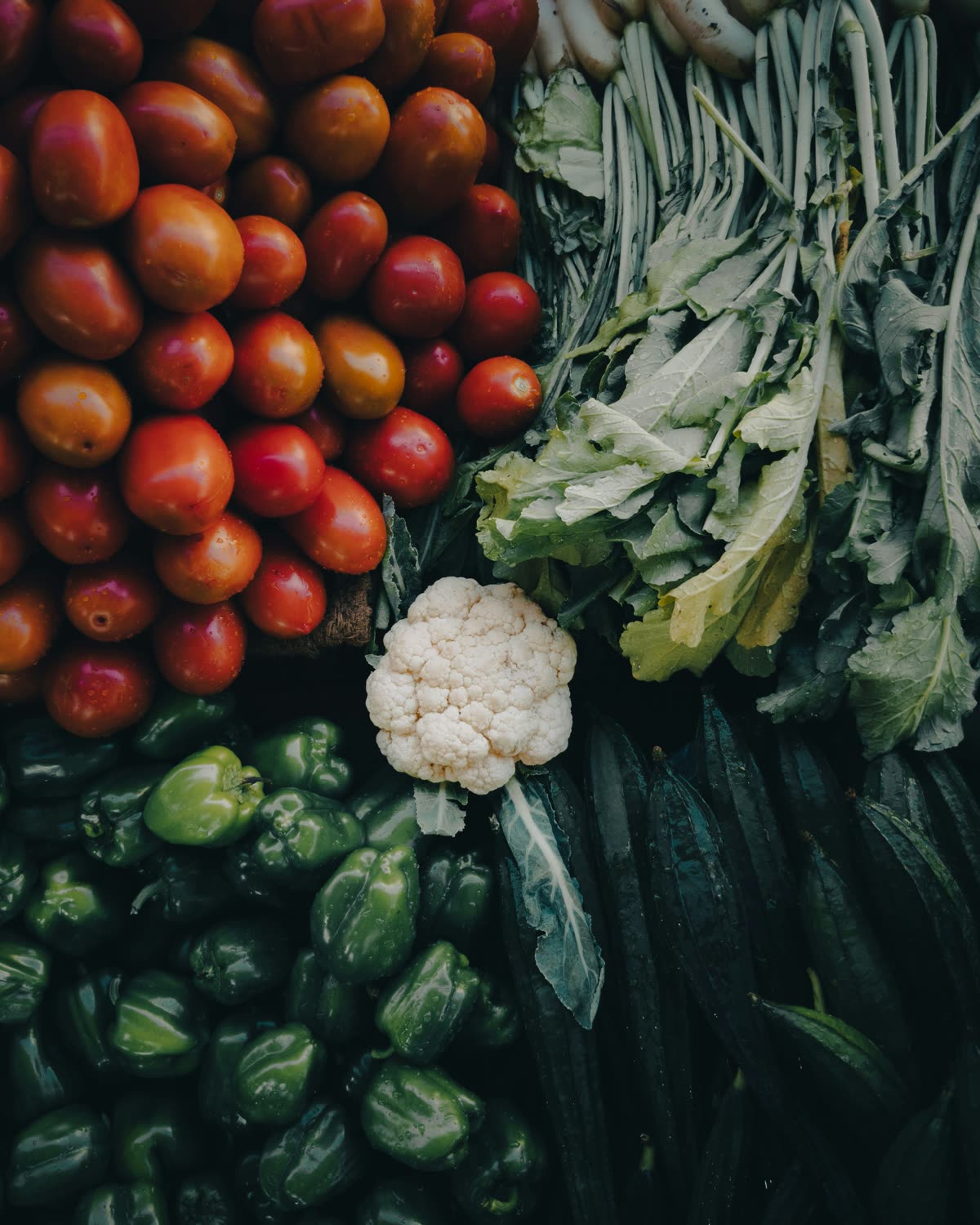 Fresh vegetables piled high: tomatoes, peppers, cauliflower and leafy greens
